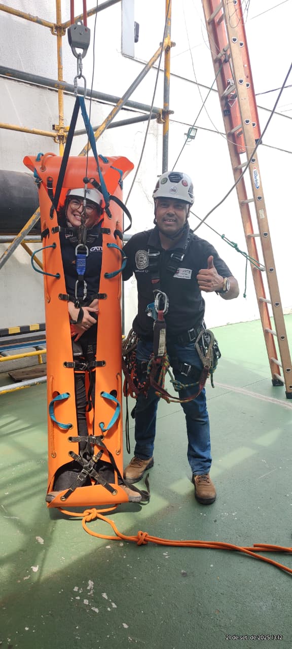 Instrutor realizando treinamento de resgate em altura com maca rígida suspensa e uso de equipamentos de segurança.