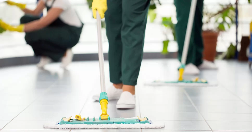 Profissional de limpeza higienizando piso com equipamento industrial.